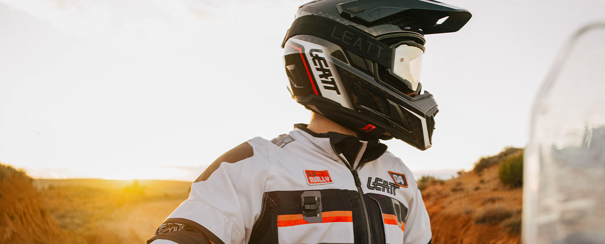 Person wearing a helmet and racing suit in a desert setting with sunset